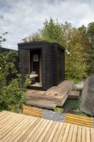 Timber wooden deck over a plunge pool - black painted wood sauna cabin with a living roof planted with wildflowers and herbs - Finnish Soul Garden