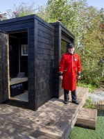 A Chelsea pensioner on press day on a timber wooden deck - black painted wood sauna cabin with a living roof 