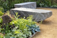 Polished surface stone boulder bench seats made from rocks on a gravel path patio area and mixed planting in the border of Hostas, Ferns, Heuchera, Alliums and Dicentra spectabilis 'Alba', syn. Lamprocapnos spectabilis 'Alba'- white bleeding heart