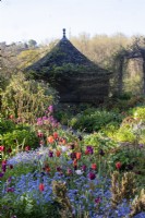 Early morning sunshine on spring borders filled with tulips and forget-me-nots looking towards a tiled summerhouse and pergola at Gravetye Manor.
