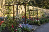 A wooden seat under an metal arbour with trained fruit trees over in the Kitchen Garden at Gravetye Manor.