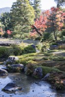 Stream in garden with rocks and view to trees with autumn colour and to hills outside the garden