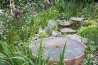 Round copper metal water feature in a wildflower garden with pond and stepping stones