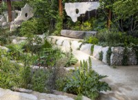 Sunken garden area with oak bench seat and reclaimed concrete sculptures suspended from rusty steel girders - mixed perennial planting 