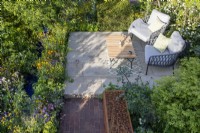 Stone paved patio seating area with table and chairs with cushions mixed perennial planting of Lychnis flos-cuculi, Trollius chinensis and Ranunculus acris
