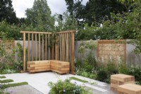 Modern contemporary patio area with grey stone paving, wooden bench seat and sweet chestnut screens on the walls, mixed perennial planting in white and green tones 