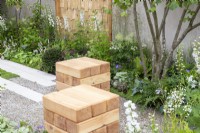 Wooden cube seats in a gravel garden surrounded by mixed perennial planting including Delphinium 'Guardian White'