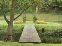 Bridge leading to moated island with metal arch and tulips
