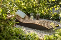 A wooden recliner with cushion in a woodland garden with mixed perennial planting 