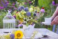 Yellow - blue - white themed bouquet consisting of Echinops, Snapdragon, Fennel, Echinacea, Achillea and Physalis in a teapot.