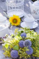 Yellow - blue - white themed bouquet consisting of Echinops, Snapdragon, Fennel, Echinacea, Achillea and Physalis on the table set for tea.