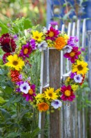 Wreath made of summer flowers and berries including Dahlia, Helianthus, Foeniculum, Calendula, Petunia, Sweet peas and Guelder rose berries hanging on a fence.