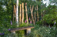 Wooden garden bench with mixed perennial planting and stripped bark tree trunks as sculptural form focal point