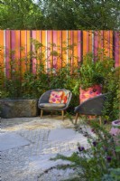 Seating area with two chairs by the wall in orange and pink colours. 
The RHS and Eastern Eye Garden of Unity, Designer: Manoj Malde, Chelsea Flower Show 2023