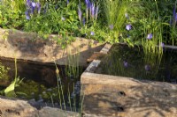 Water rills made from reclaimed timber sleepers with a metal water spout -  mixed perennial planting Geranium 'Johnson's Blue'