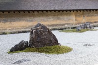 The Rock Garden with raked gravel and placed stones in moss islands. Walls of clay with tiled roofs. 