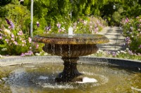 A fountain in a carved stone urn surrounded by summer borders at RHS Garden Wisley.