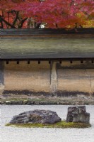 The Rock Garden with raked gravel and placed stones in moss island. Walls of clay with tiled roofs. Acers in autumn colour outside the garden. 