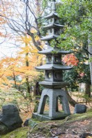 Tall stone pagoda with trees in autumn colour behind. 