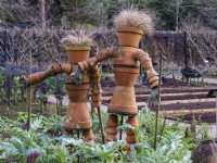 A pair of gardeners made from terracotta pots stand amongst raised beds at RHS Rosemoor Garden in February.