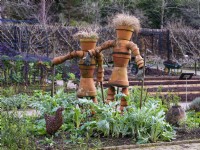 A pair of gardeners made from terracotta pots stand amongst raised beds at RHS Rosemoor Garden in February.
