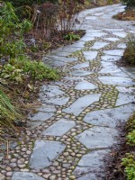 Winding garden path made of river cobblestones and slate, February.