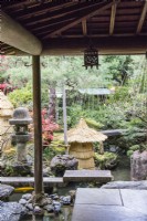 View from veranda to stone bridge crossing water with straw-wrapped fragile stone ornament as protection against frost. Shrubs with pole and rope protection against snow damage called Yukitsuri. Stone lantern called Ishidoro.