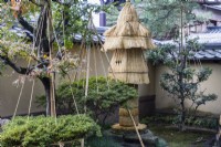 Courtyard with shrubs within wigwams of rope and bamboo as protection against snow damage. Also fragile stone ornament wrapped in decorative straw covering to prevent frost damage. 
