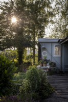 Converted railway carriage with wooden deck, Sun setting behind mature trees