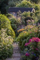 Over flowing summer borders with Roses, Day Lilies, Lavender and Astrantia 'Buckland', paved path between