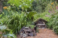 Nature friendly garden with a small insect hotel and hedgehog shelter made from cones, logs, bamboo and moss.
Plants include; Hemerocallis - daylily,  Gunnera manicata - Giant rhubarb and Astilbe