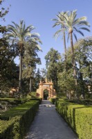 Clipped hedges line a brick path leading to an ornate pavilion within the Jardines de las Damas. Real Alcazar Palace gardens, Seville. Spain. September. 
