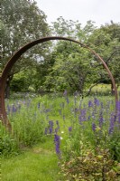 A mown path through a Corten steel moon gate in a perennial wildflower meadow.
