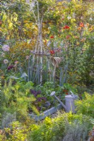 Autumn bed with vegetables, watering can and garden fork with hat on the handle.