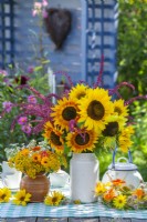 Summer wreath and bouquets with sunflowers, amaranthus, nasturtium, pot marigolds and tansy in vases on the table.