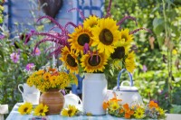 Summer wreath and bouquets with sunflowers, amaranthus, nasturtium, pot marigolds and tansy in vases on the table.