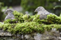 Stone birds on a wall covered with moss in a winter garden