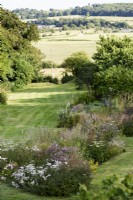 View across borders of herbaceous perennials towards the surrounding landscape in a country garden in July