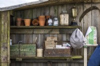 Wooden antique boxes with vintage gardening books, packets of seeds and clay pots, garden twine and jars stand on shelves in a wooden shed
