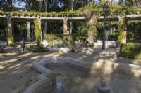 A stone fountain in front of a large curving pergola. Parque de Maria Luisa, Seville, Spain. September