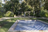 A blue and white tiled pool with two fountains' large curved pergola is in the background. Parque de Maria Luisa, Seville, Spain. September