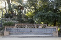 A wide, curving, low colourful tiled bench, with a mound behind with pergola on the top. Mudejar, Islamic style bench. Parque de Maria Luisa, Seville, Spain. September