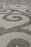 A large, flat open area is cobbled in black and white pebbles and laid out in a symmetrical and geometric pattern. Plaza de Espana, Parque de Maria Luisa, Seville, Spain. September