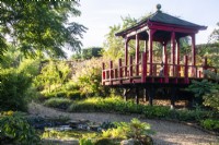 The wooden pagoda in The Thai Garden at The Manor, Little Compton, with a small pond in the foreground and planting that includes bamboo and hakonechloa.