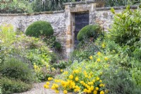 Perennials spill onto a gravel path that leads to a door set into a stone wall at The Manor, Little Compton.