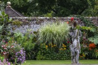 A statue stands in front of mixed planting in the Swimming Pool Garden borders with grasses, cannas and perennials.