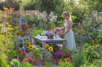 A woman adds a wreath made of summer flowers to a table ready for tea.