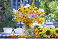 Summer flower bouquet with Rudbeckia, Tropaeolum majus, Solidago and Malva in a glass jar decorated with twine.