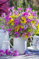 Pink yellow bouquet in white vase containing sweet peas and helianthus.