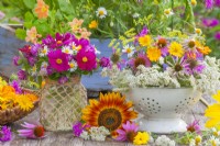 Floral arrangement with bunch of Cosmos, Chamomile and Red Clover in a glass jar decorated with twine and a colander full of harvested medicinal and herb flowers including Pot marigolds, Coneflowers, Bergamot, Fennel, Chamomile and Yarrow.